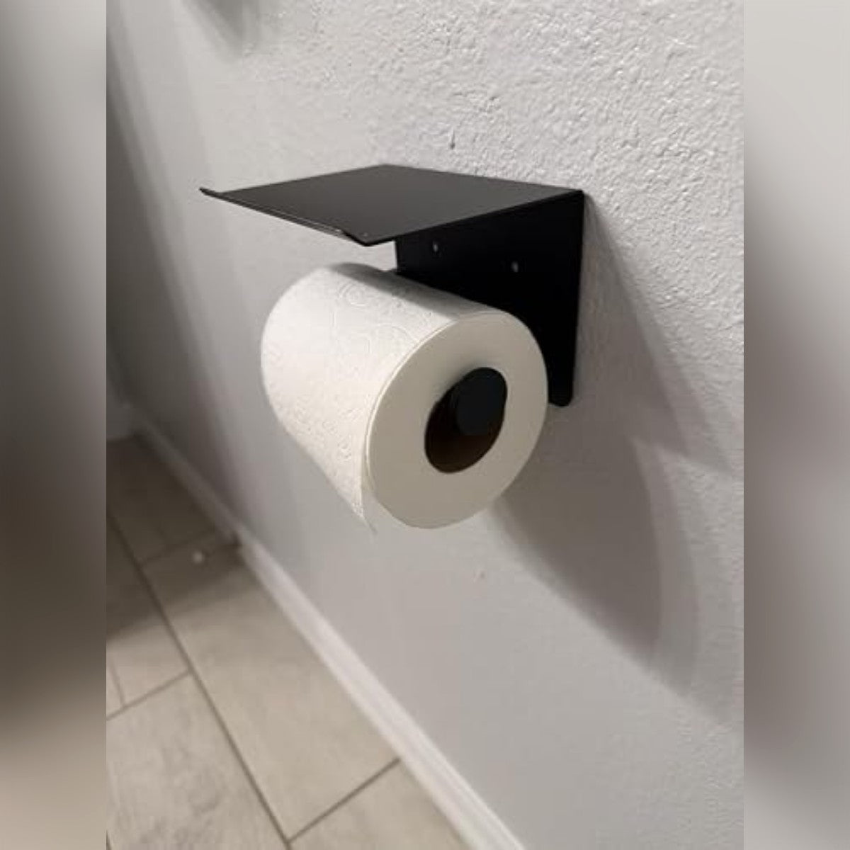 Köparens foto: den svarta toalettpappershållaren med hylla på en ljus vägg, med en toarulle på armen